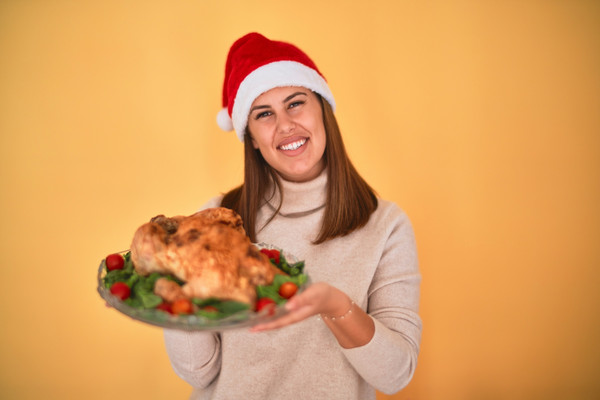 KI generiert: Eine Person mit Weihnachtsmütze hält einen Teller mit einem gebratenen Truthahn und frischem Gemüse. Die Szene vermittelt eine festliche Stimmung.